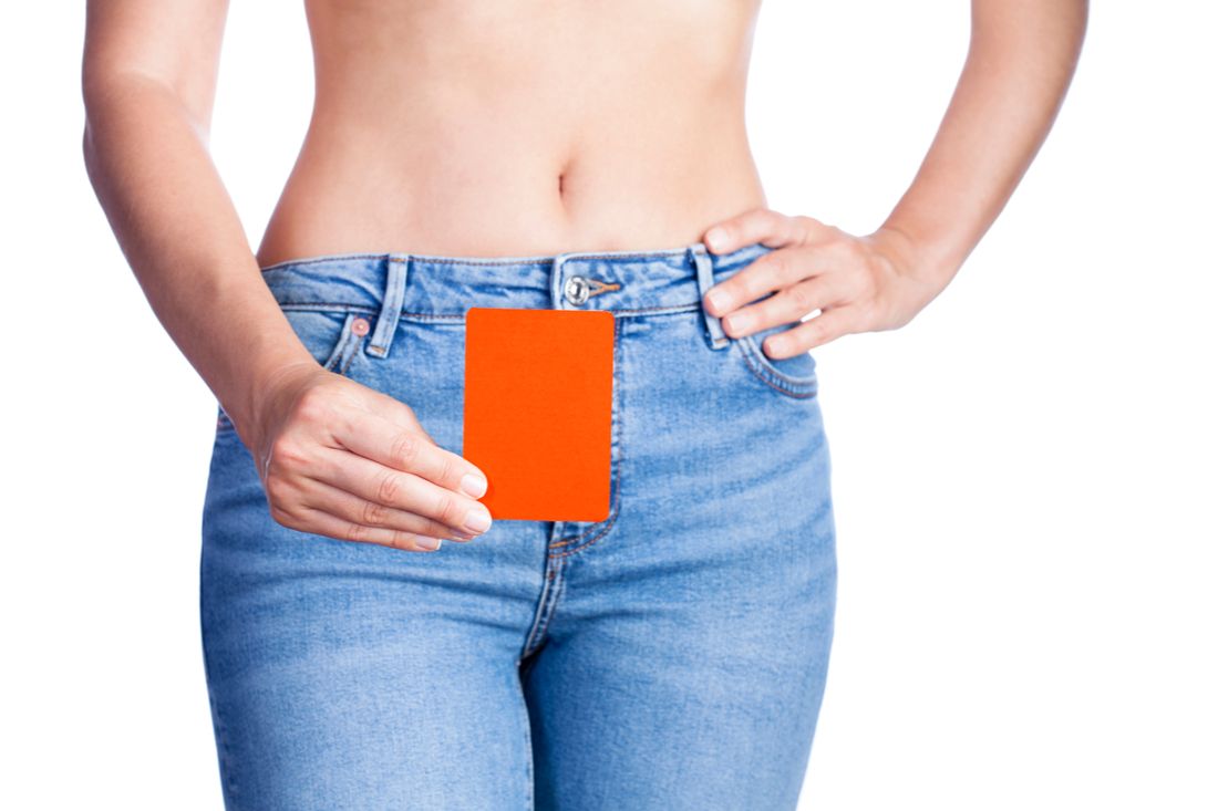 Vaginizmus - mladá žena drží červenú kartu pred pohlavím