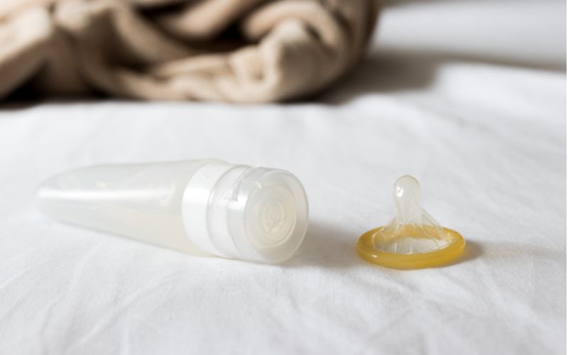 Lubrikačné gély a sex, fľaštička s lubrikantom a kondóm na posteli