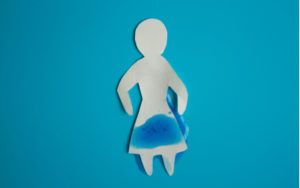 Inkontinencia - papierová žena na modrom pozadí a premočením v intímnej oblasti